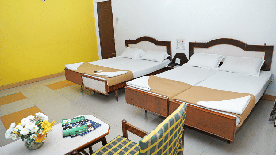 A spacious room at Hotel Vikram with 2 neatly made beds and a yellow accent wall and a seating area.