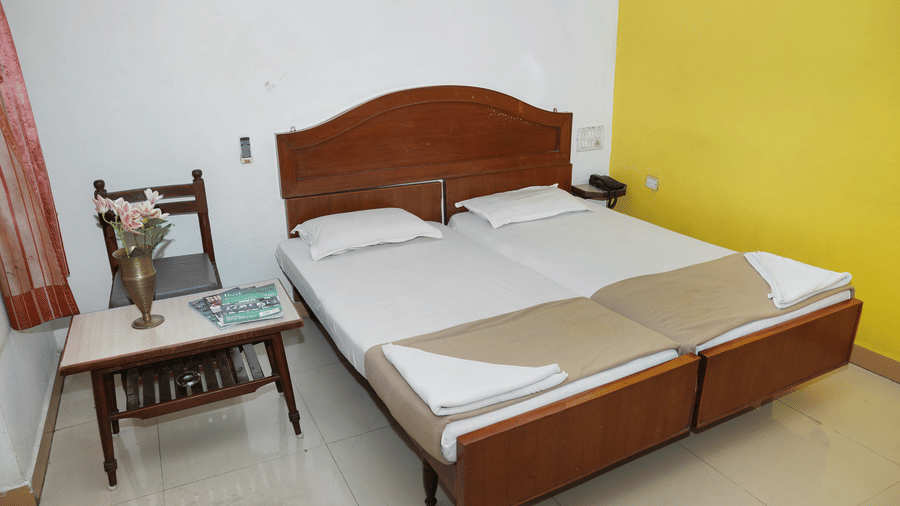 A minimalist double room at Hotel Vikram with wooden headboards and a small side table with chair.