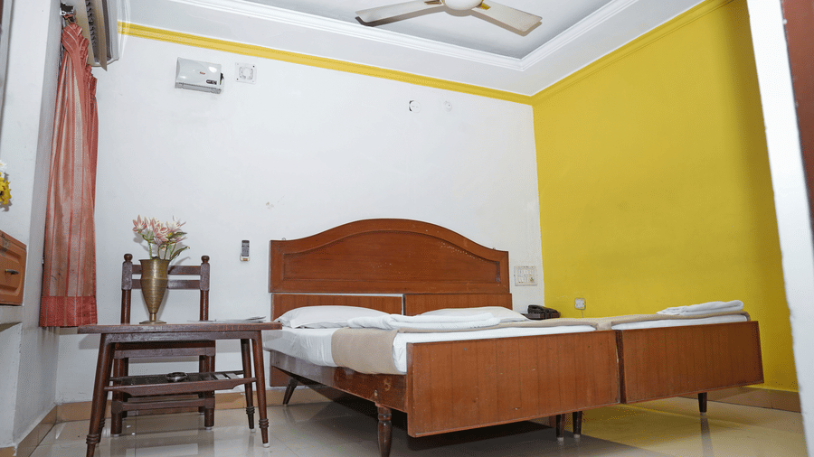 Low-angle view of a double bedroom at Hotel Vikram showing the ceiling fan and minimalist decor.