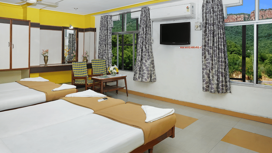 A bright twin bedroom at Hotel Vikram featuring a large window with a scenic view of green hills.