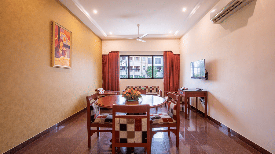 A well-lit dining space within a guest suite featuring a round table and checker-ed upholstered chairs - Jenneys Residency, Coimbatore