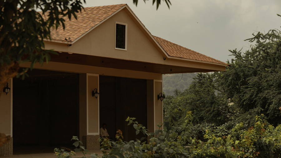 A small house with a sloped roof and front porch, surrounded by greenery, with a visible doorway and windows under an overcast sky at Jivana Wellness Retreat, Bhopal.