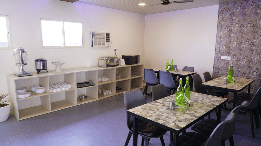 Dining area of Lime Tree Hotel, Pulkit featuring multiple tables, chairs, and a shelving unit.
