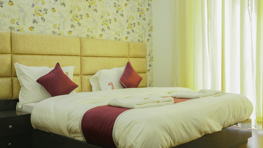 Bedroom of Lime Tree Hotel, Pulkit featuring floral wallpaper, a beige headboard, and a maroon throw.