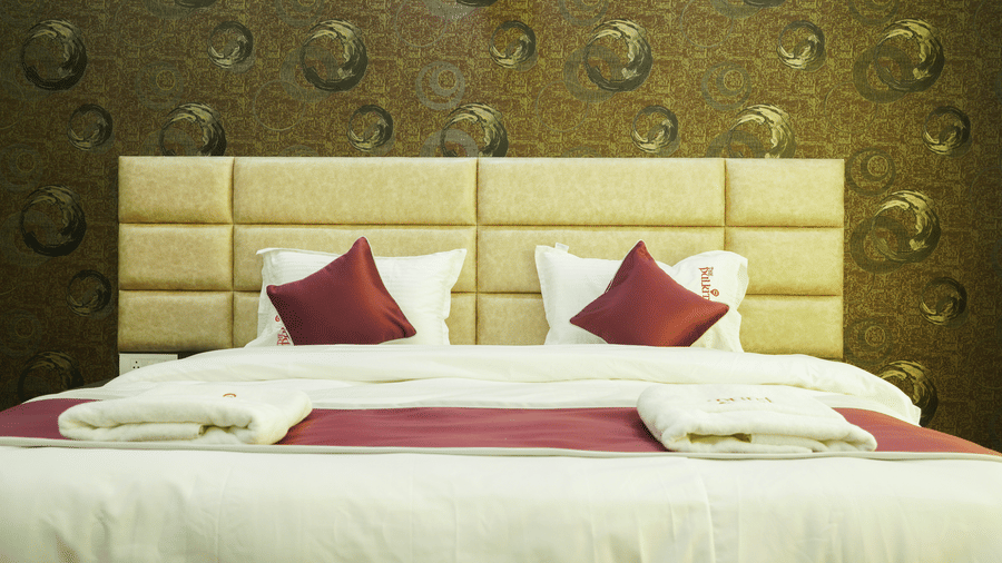 Bedroom of Lime Tree Hotel, Pulkit featuring a textured beige headboard and maroon bedding.