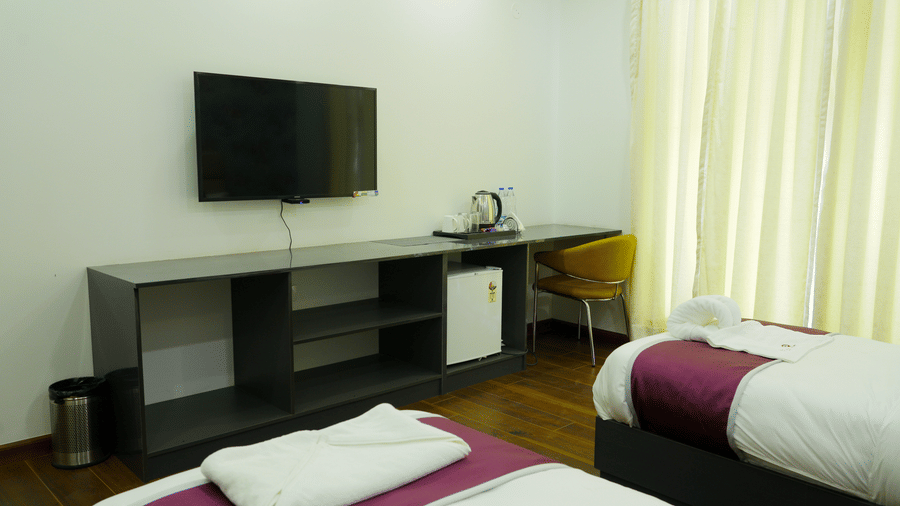 Bedroom of Lime Tree Hotel, Pulkit featuring a wall mounted television, a console, and maroon bedding.