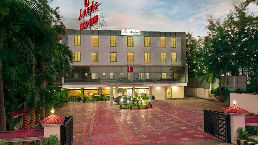 The exterior of a modern hotel with a red and white flag and landscaped entrance - Lords Eco Inn Dahej