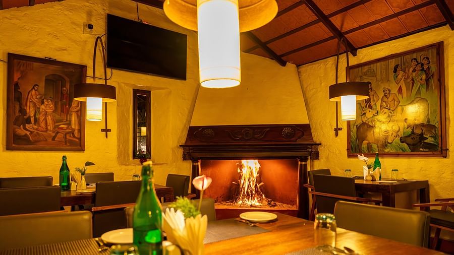 Warmly lit dining area with wooden furniture and decorative wall art. | Mango Hill, Yercaud