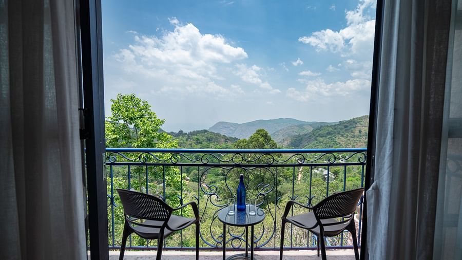Balcony with two chairs and a table offering a scenic view of green mountains and a bright blue sky.  | Mango Hill, Yercaud