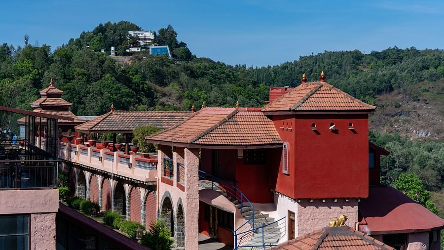 A scenic view of a hotel building with red roofs, surrounded by lush greenery and hills.  | Mango Hill, Yercaud