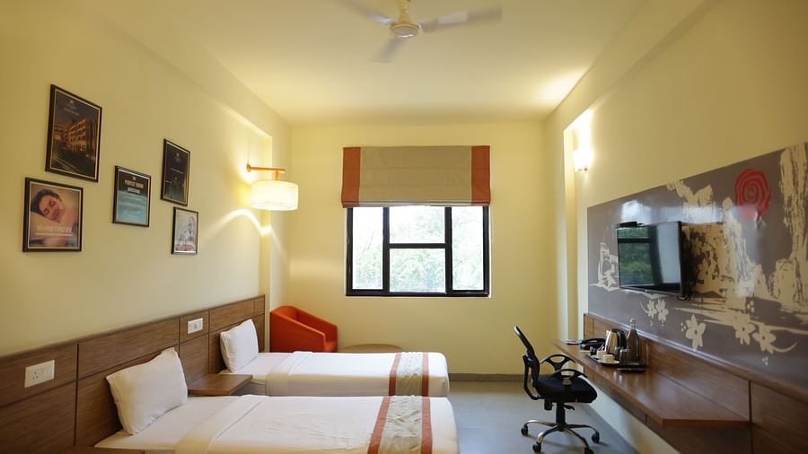 full view image of a room featuring the single beds placed opposite the television along with a window and a cushioned armchair in the far end - Max Hotel Jabalpur