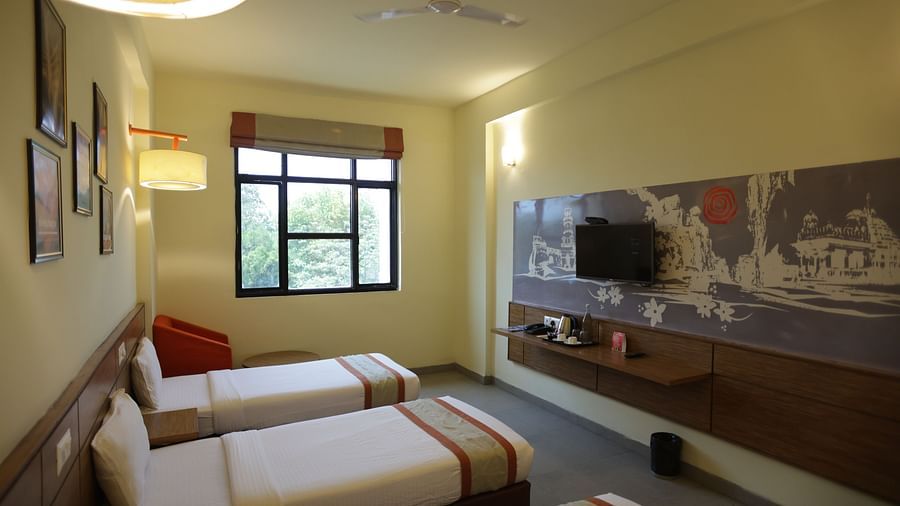 corner view image of a room with three single beds facing towards the wall mounted television - Max Hotel Jabalpur