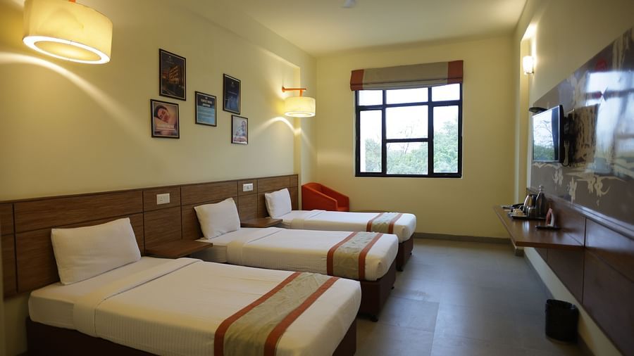 a neatly kept room with three comfortable single beds with small photo frames hung on the wall behind them - Max Hotel Jabalpur
