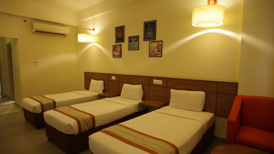 a room with warm lighting featuring three single beds along with a wall mounted air-conditioning - Max Hotel Jabalpur