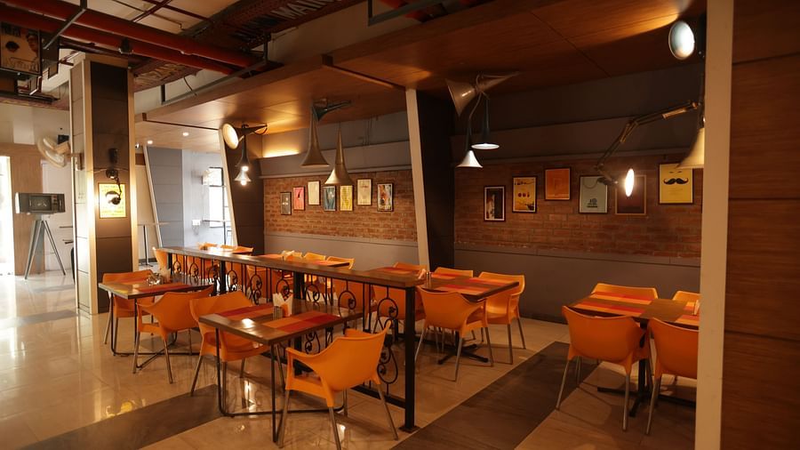 corner view image of a dimly lit dining area with chairs and tables arranged with chic interiors - Max Hotel, Jabalpur