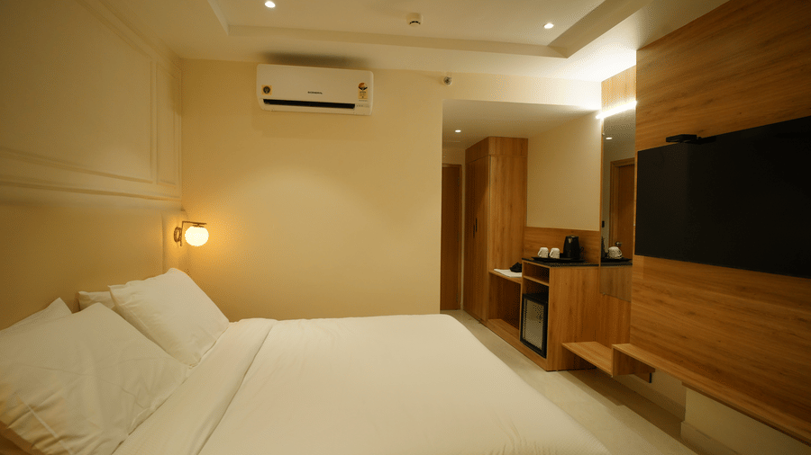 Clean, bright guest room at Monday Premium, Madhapur, featuring a large bed with white bedding and a wall-mounted TV over wooden cabinetry.