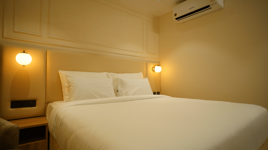  Close-up of a double bed at Monday Premium, Madhapur, showing crisp white linen, padded headboard, and warm bedside lighting.