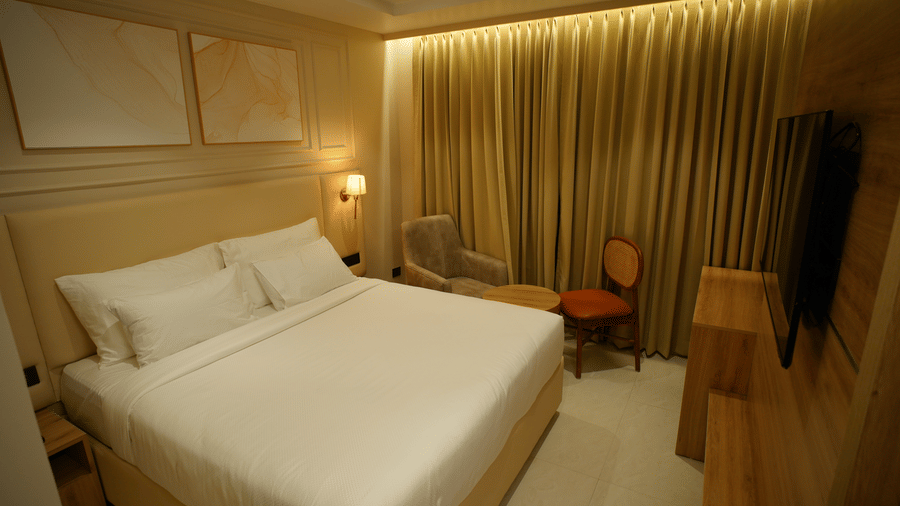  King size bed in a spacious guest room at Monday Premium, Madhapur, featuring framed artwork and gold, draped curtains. 