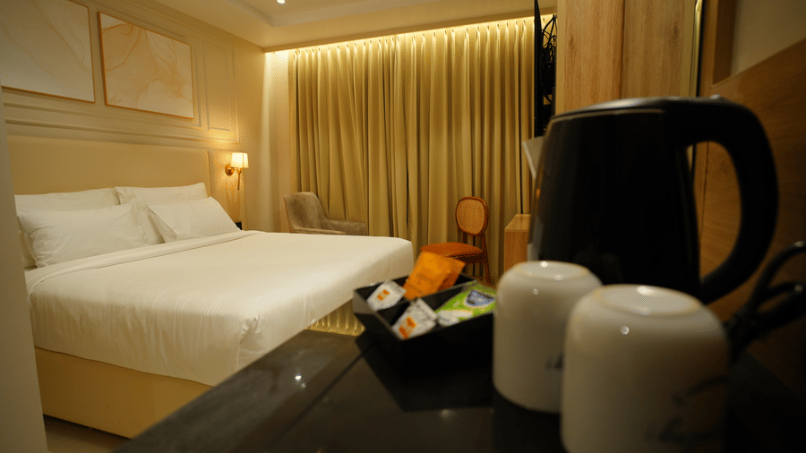  Tea-making area in a guest room at Monday Premium, Madhapur, showing a kettle and mugs up close, with a king-sized bed in the background. 