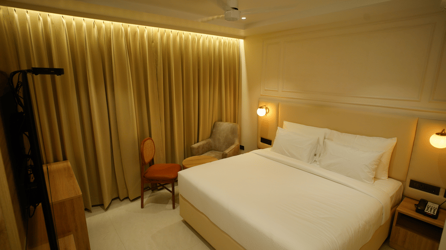  Inviting double room at Monday Premium, Madhapur, featuring a large bed with white linen and floor-to-ceiling gold draped curtains.