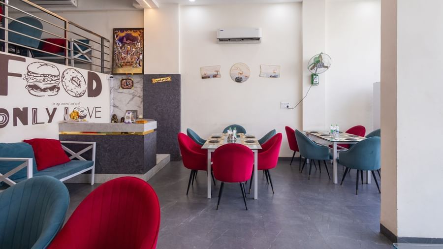 Dining area with red and blue chairs, tables, and wall art at Pravasa Stay Dewas Naka, Indore.