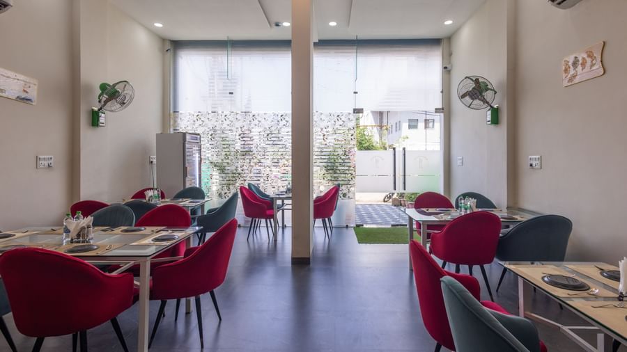 Bright dining hall with glass doors, tables, and red chairs at Pravasa Stay Dewas Naka, Indore.