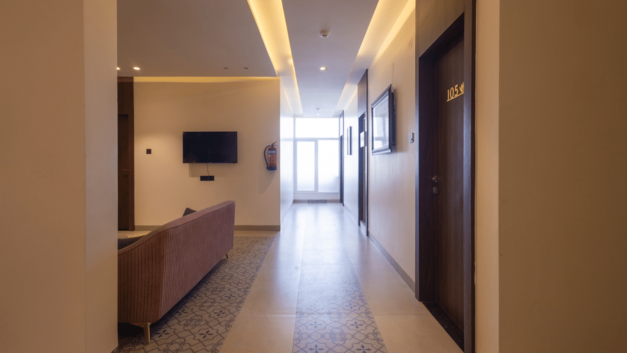Interior view of a hallway leading from the lobby area with a television on the wall at Pravasa Stay Luv Kush, Indore.