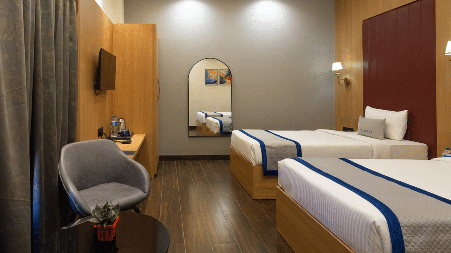 Interior of a guest room with 2 single beds, seating, and a rounded mirror at Pravasa Stay Luv Kush, Indore.