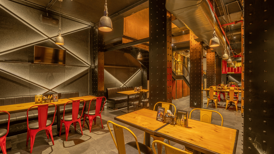 A modern industrial style bar features chairs and wooden tables beneath exposed ceiling beams at S Hotels, Chennai.