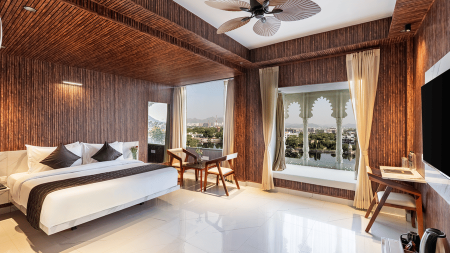 Bright, modern hotel room with a double bed, dark wooden walls, and a large window offering a scenic waterfront view.