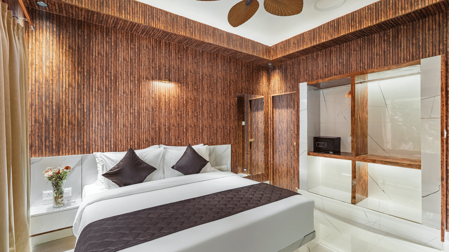 Elegant hotel room with a double bed, dark cushions, wood panelling, and a contemporary wardrobe/storage unit.