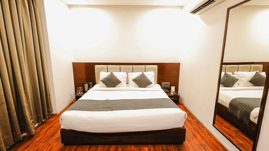 Executive Room at TGI Apple Inn, Ajmer Road, Jaipur featuring a bed with pillows, a mirror on the wall, curtains, and tables.