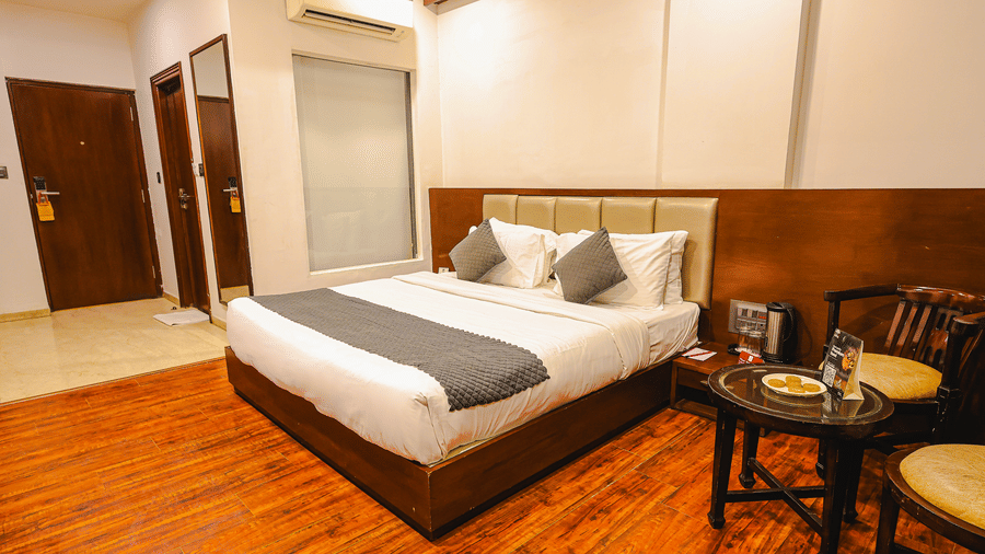 Royal Executive Room at TGI Apple Inn, Ajmer Road, Jaipur featuring a bed with pillows, chairs around a table, doors, mirror, and air conditioner.