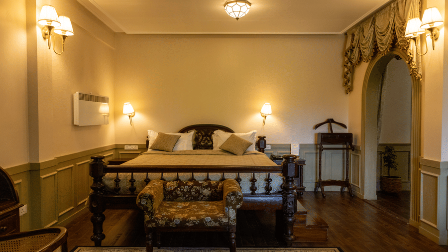 A room at The Heritage Club, Tripura, Castle, Shillong, showcasing large bed, pillows, spreads, lamps, a table, and a carpet.