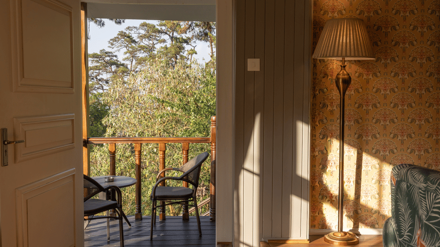 A room at The Heritage Club, Tripura, Castle, Shillong, featuring a door to the balcony with chairs.