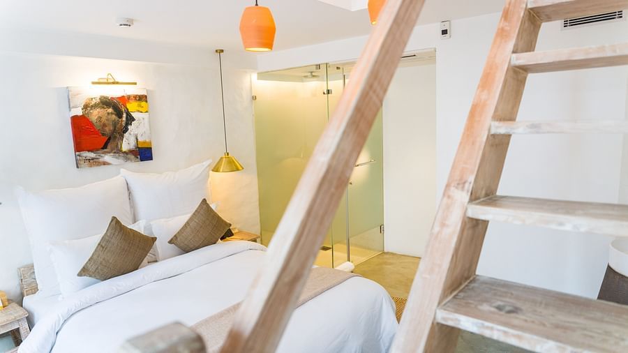 Deluxe loft room with a bed, bamboo lamps hung from the ceiling and art work on the wall - The Nanee