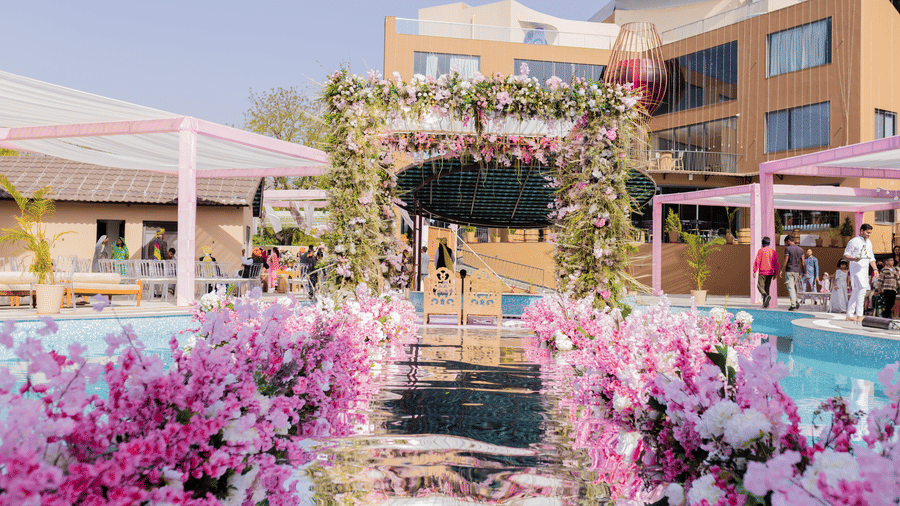 An outdoor venue showcases floral decor around a pool area and buildings | The Qualia Resort Club & Brewery, Udaipur