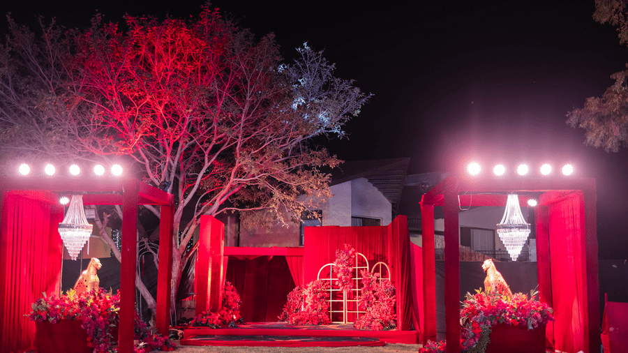 A stage is dramatically lit in red, flanked by trees and decorative elements | The Qualia Resort Club & Brewery, Udaipur