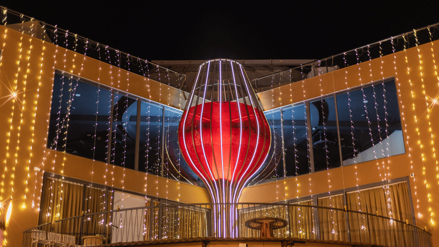 A large red heart-shaped glass decoration hangs in a modern building at night for a wedding | The Qualia Resort Club & Brewery, Udaipur