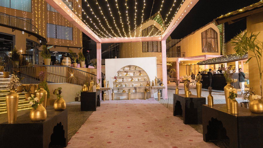 An indoor wedding reception area is decorated with lights, flowers, and tables with food | The Qualia Resort Club & Brewery, Udaipur