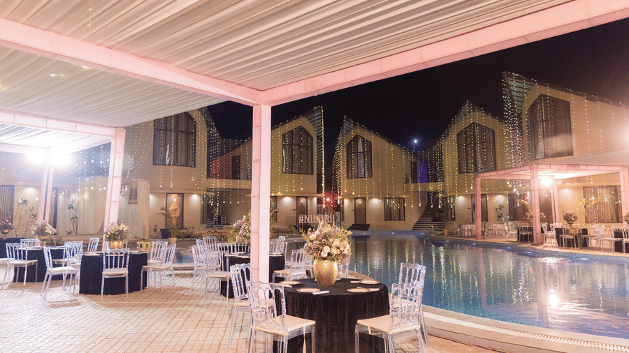 An outdoor wedding reception area is set up next to a pool at night with tables and chairs under a canopy | The Qualia Resort Club & Brewery, Udaipur