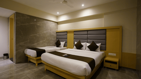 A well furnished room with a single bed and a twin size bed, featuring white linens and brown accents, dark headboards, and a bedside table at Shyanu Lords Eco Inn Airoli.