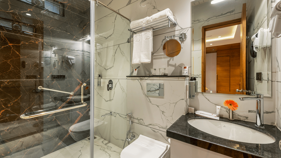 Lords hotels & resorts exhecutive bathroom that exudes elegance and cleanliness with marble finishes, a glass shower enclosure, contemporary fixtures, and well-organised amenities.