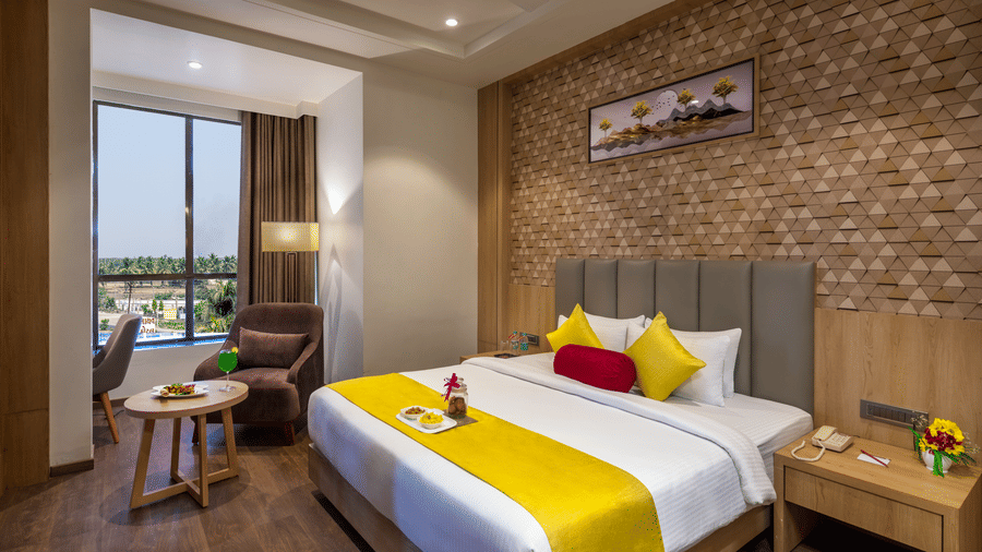 A premium room in Lords Inn Somnath with modern interiors, featuring a neatly made double bed and a large window offering a view of the outdoors.
