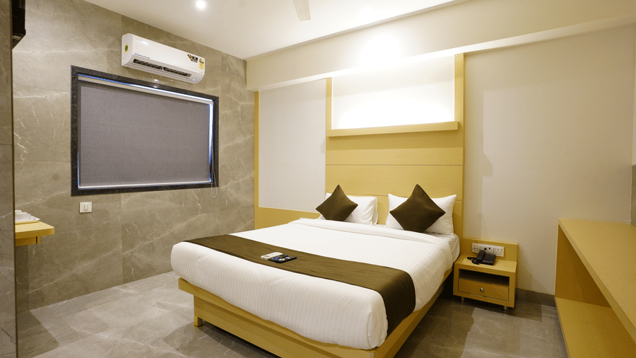 Cosy room with a double bed, white linens, brown runner, two brown pillows, and a projector screen and an A.C. at Shyanu Lords Eco Inn Airoli.