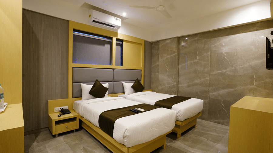 A modern designed room with two single beds, bedside tables, and wooden furniture at Shyanu Lords Eco Inn Airoli.
