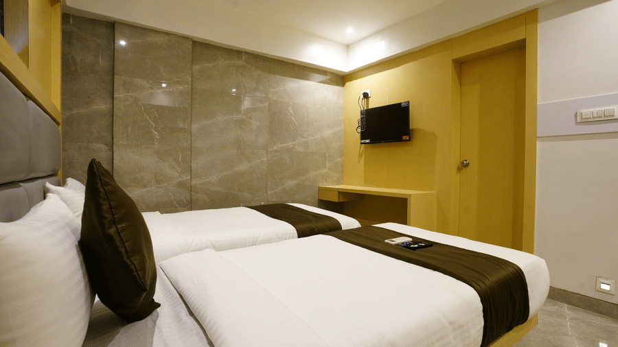 A well furnished room with two single beds, white linens, brown runners, and a wall-mounted television at Shyanu Lords Eco Inn Airoli.