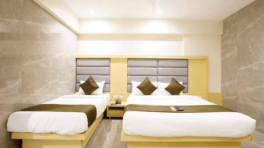 A well furnished room with one single bed and a twin size bed with light wooden headboards at Shyanu Lords Eco Inn Airoli.