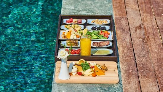 a tray of assorted foods placed on the edge of a clear water pool