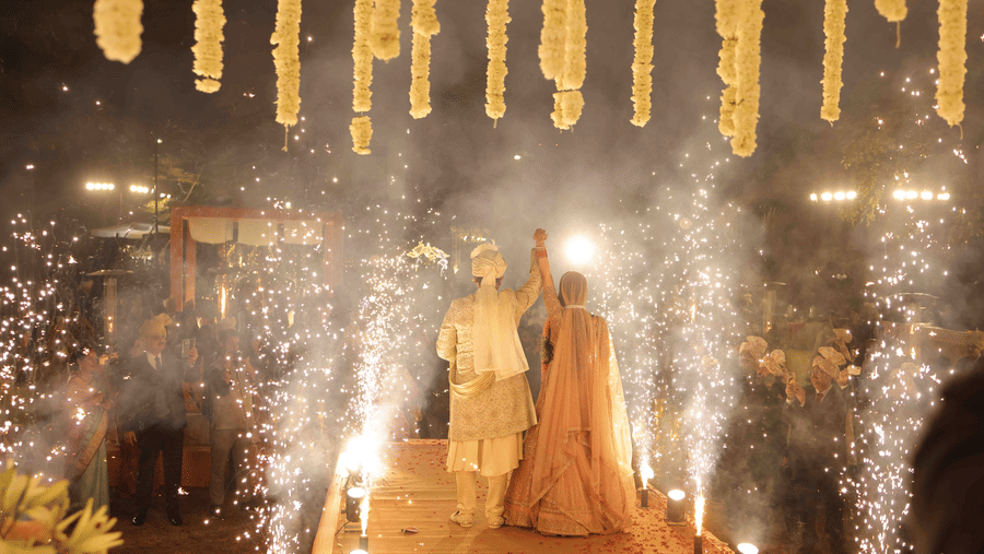 The bride and groom making a spectacular wedding entrance along a decorated walkway as sparkling pyrotechnics illuminate the celebration and guests look on | Clarks Amer, Jaipur